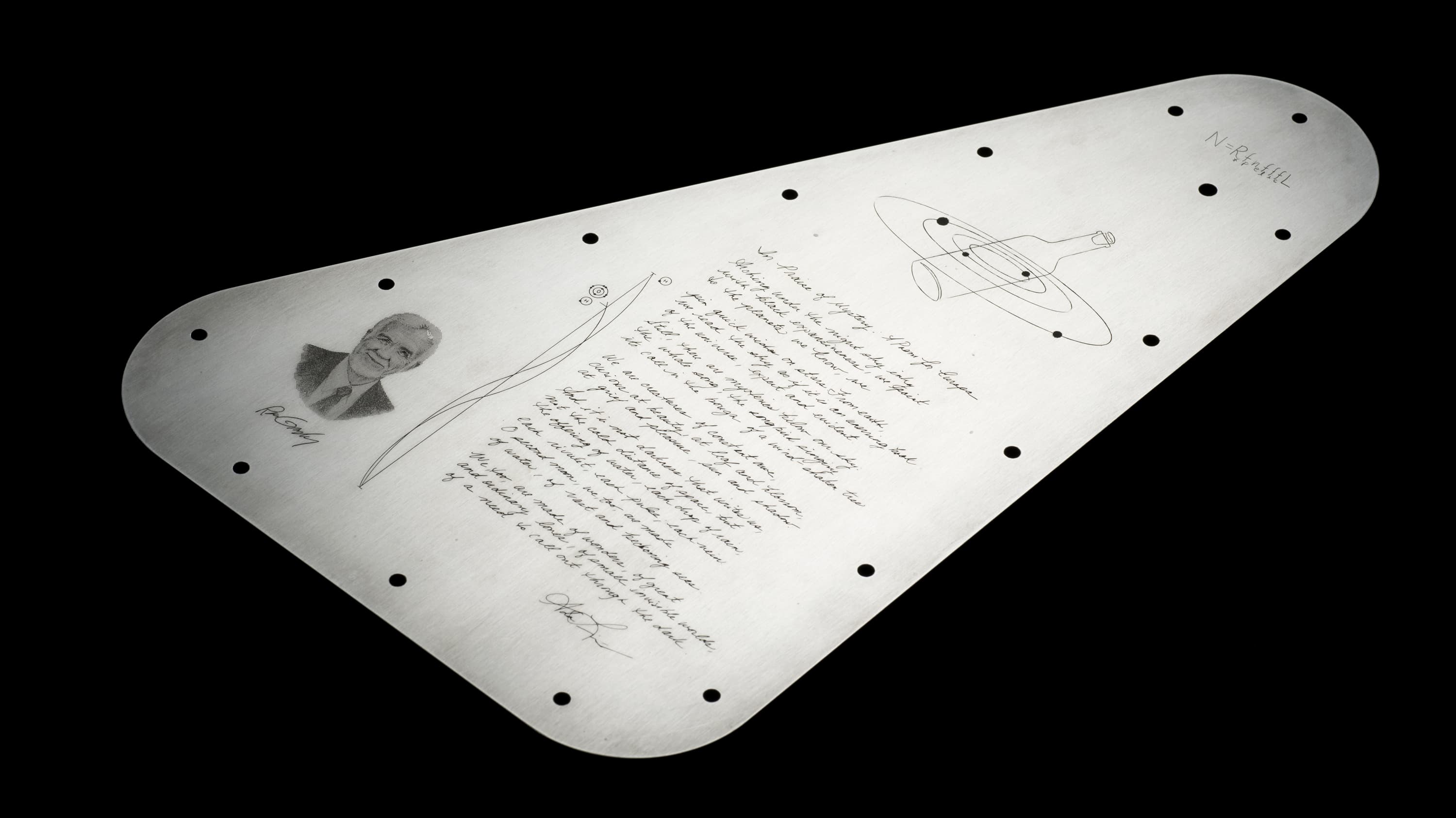 This side of the Europa Clipper's vault plate showcases a rich tapestry of scientific and cultural significance. At the top left, a detailed engraving of Frank Drake accompanies the Drake Equation in his own handwriting. Below, the graceful script of 'In Praise of Mystery: A Poem for Europa' by Ada Limón stretches across the plate. To the bottom left, a likeness of Ron Greeley pays homage to his contributions to planetary science. The 'Water Hole' radio emission lines are elegantly represented, symbolizing our search for extraterrestrial communication. This assembly of engravings on the reflective silver surface, set against the darkness, encapsulates humanity's quest for understanding beyond our world.